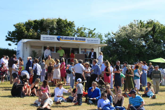 Photograph of relaxed crowds eating icecream and sitting on grass at Kinsale Point to Point